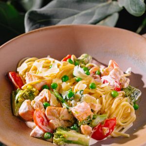 Pasta cremosa con guisantes, brócoli, salmón y tomate