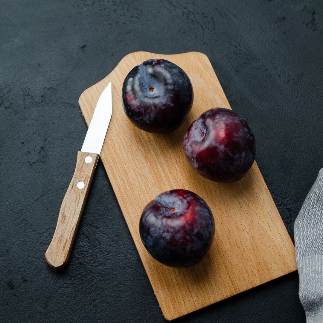 Ciruelas rojas frescas sobre tabla de madera para cortar