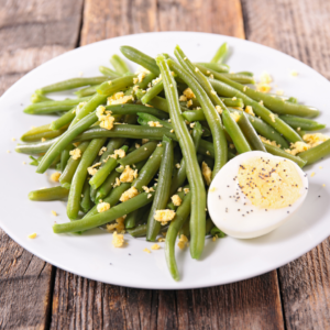 Judías verdes cocidas con huevo y migas de yema en plato blanco