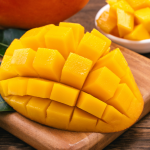 Medio mango cortado en cubos estilo erizo sobre tabla de madera, listo para servir.