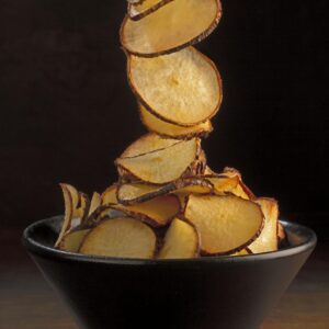 Chips de yuca al horno en bol negro con yuca fresca al fondo