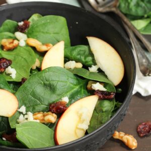Ensalada de espinacas, manzana y nueces peladas en bol negro